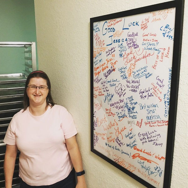 Jessica standing next to wall with white board that has good luck notes written on it