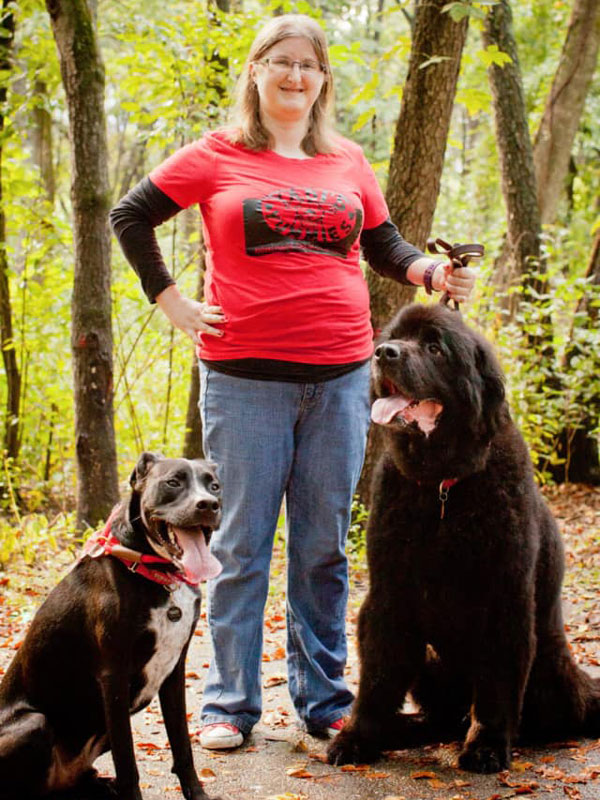 Jessica standing in forest with her two dogs, Yadi on her left and Annie on her right